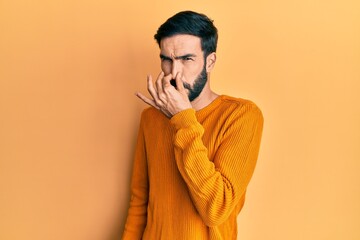 Young hispanic man wearing casual clothes smelling something stinky and disgusting, intolerable smell, holding breath with fingers on nose. bad smell