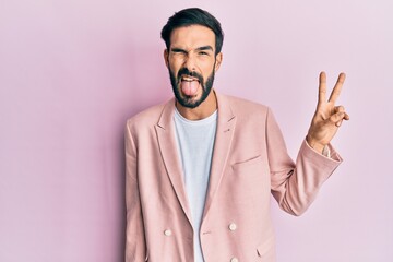 Young hispanic man wearing business jacket smiling with happy face winking at the camera doing victory sign. number two.