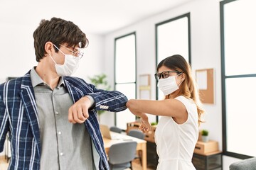 Two business workers wearing medical mask doing elbow coronavirus handshake at the office.