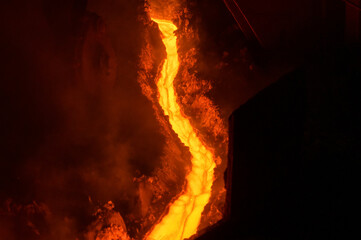 A stream of hot metal, molten steel flowing along a guide chute.