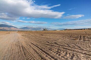 Tractor tracks on a farmland with a background of mountain range and lake in Saratoga Springs, Utah