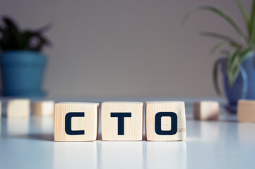 CTO word written on wood block. CTO - chief technology officer - word is made of wooden building blocks lying on the yellow table. CTO, business concept, blue background