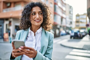 Young hispanic business woman wearing professional look smiling confident at the city using...