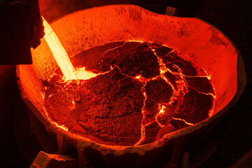 A jet of molten metallurgical slag is poured into a large ladle.
