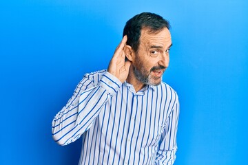 Middle age hispanic man wearing casual clothes smiling with hand over ear listening an hearing to rumor or gossip. deafness concept.