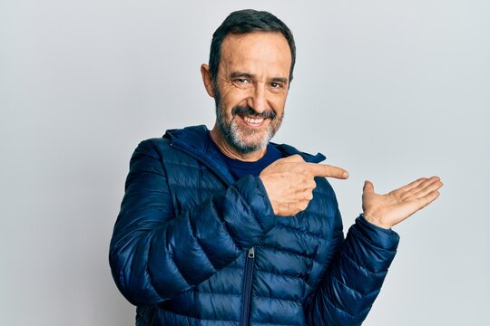 Middle age hispanic man wearing casual clothes amazed and smiling to the camera while presenting with hand and pointing with finger.