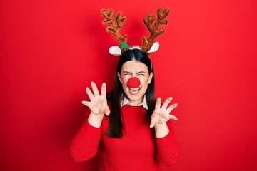Young hispanic woman wearing deer christmas hat and red nose smiling funny doing claw gesture as cat, aggressive and sexy expression