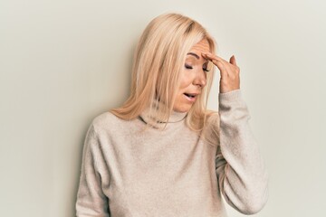 Young blonde woman wearing casual winter turtleneck sweater surprised with hand on head for mistake, remember error. forgot, bad memory concept.