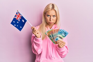 Young blonde woman holding australian flag and dollars skeptic and nervous, frowning upset because of problem. negative person.