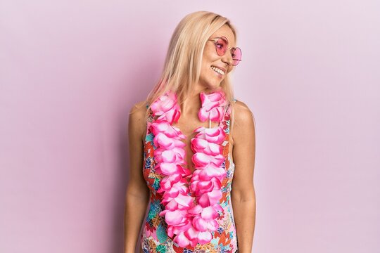 Young blonde woman wearing swimsuit and hawaiian lei looking away to side with smile on face, natural expression. laughing confident.
