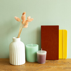 Notebook, candle, vase of dry flowers on wooden desk. green wall background. workspace