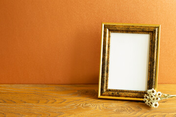 Empty picture frame with dry flowers on wooden table. orange wall background. home interior