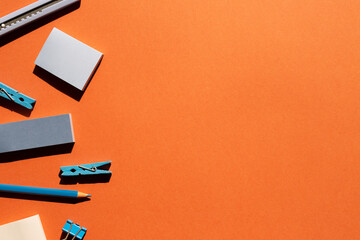 Blue memo notepad, clips, cutter, colored pencil on red background. Work and study place. flat lay, top view, copy space