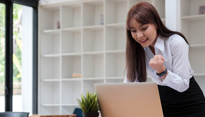 Photo of a cheerful business woman standing in a conference room with a laptop computer. looking aside make winner gesture.