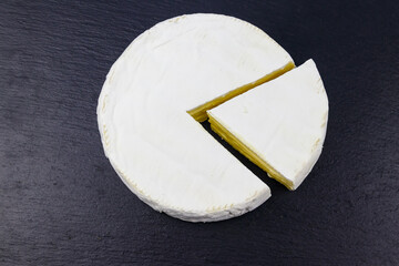 Brie cheese on a black slate background. Top view