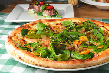 Delicious pizza with spinach and tuna shavings served on wooden table with green plaid tablecloth.