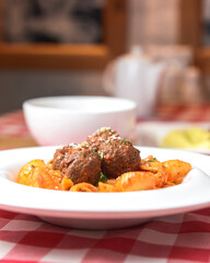 Macaroni dinner with meatballs. Meat pasta served in a white plate over red plaid tablecloth.