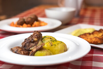 Grilled meat with baked potatoes. Served on a white square plate over red plaid tablecloth.