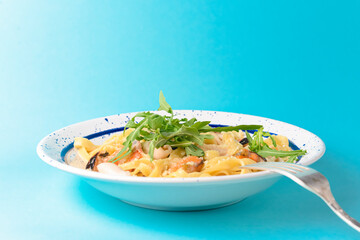 Traditional Italian pasta with clams and ruccola served in a white plate over blue background.