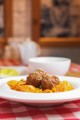 Penne pasta with meatballs in tomato sauce in a white bowl. Top view. On rustic wooden table with red plaid tablecloth.