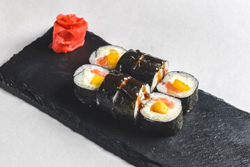 Fresh salmon sushi rolls with pickled ginger and wasabi on a black plate over white background.