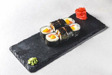 Fresh salmon sushi rolls with pickled ginger and wasabi on a black plate over white background.