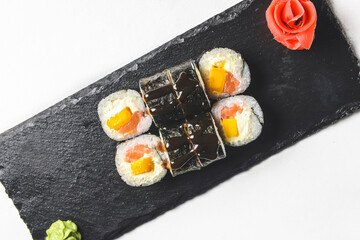 Fresh salmon sushi rolls with pickled ginger and wasabi on a black plate over white background.