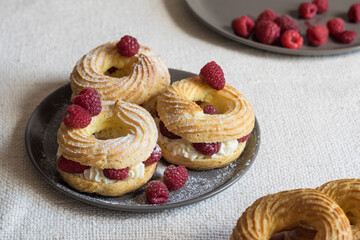 Cream puff rings eclairs choux decorated with fresh raspberries on grey plate, selective focus
