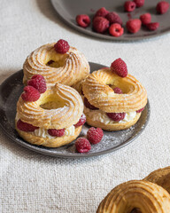 Cream puff rings eclairs choux decorated with fresh raspberries on grey plate, selective focus