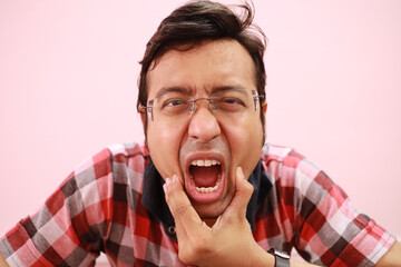 Indian man in checkered clothes having an acute toothache while putting pressure on his jaw