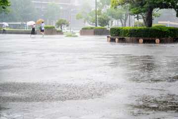 激しい雨の降る街　傘をさして歩く人