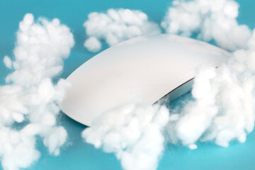 Wireless mouse surrounded by cotton balls on blue background