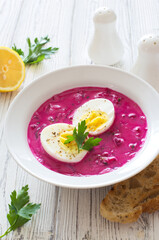 Cold beetroot cucumber egg soup in white bowl close up