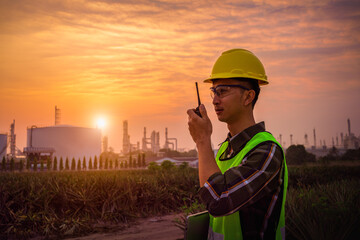 A construction engineer, a young engineer holding a radio and wearing a helmet standing in front of the refinery, exploring new plans and expanding the factory, Silhouette engineer standing.