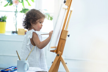 Two years old girl paint on canvas standing on the easel in her room at home, early childhood education concept