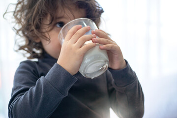 Curly toddler girl enjoying and drinking milk with glass