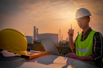 Construction surveyor, a young engineer holding a radio and wearing a helmet standing in front of the refinery, exploring new plans and expanding the factory, Silhouette engineer standing.