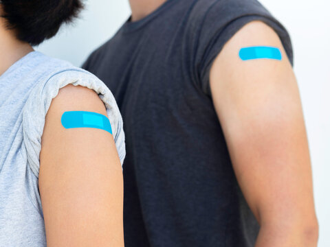 Vaccinations, bandage plaster on vaccinated people concept. Blue adhesive bandages on a woman's shoulder who wearing grey shirt next to a man in dark shirt, after vaccination treatment.