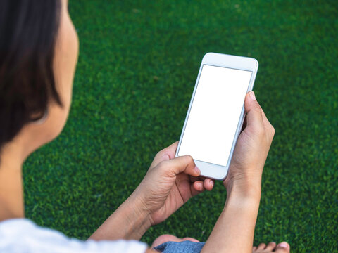 Mockup image of phone. Close-up white blank screen on mobile phone in hands on green artificial grass background. Hand holding white smartphone with empty screen.