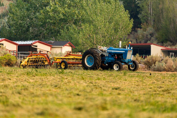 Fototapeta na wymiar Old blue tractor attached to hay machinery parked in a field