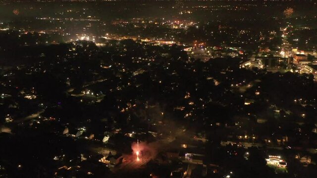 An aerial view of the 2021 Fourth of July fireworks set off by the locals on Long Island, NY. The drone camera dolly in and tilt down over the suburban neighborhood as fireworks go off below.