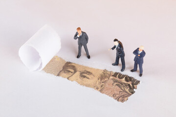 Three businessmen dolls standing beside torn holes on white background leaking Japanese yen bills