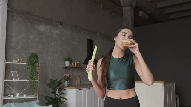 Brunette Woman Is Eating A Burger While Holding A Natural Leek In Hand At Home