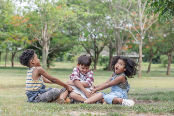 Fototapeta premium Multi-ethnic children sitting on lawn and fight pulling for a laptop to play game.