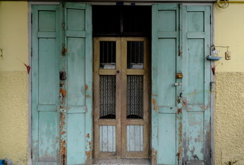 Weathered green shutters open on doors with iron bars