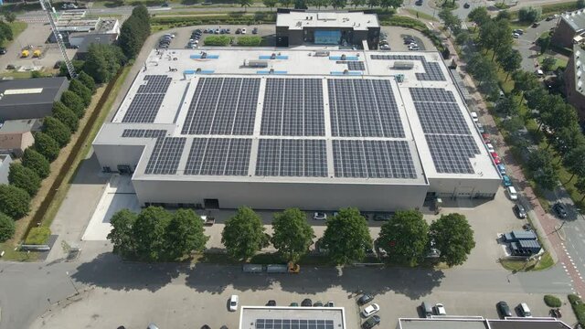 Drone pulling back from industrial buildings with photovoltaic solar panels on rooftop. Revealing multiple office building being supplied with green energy