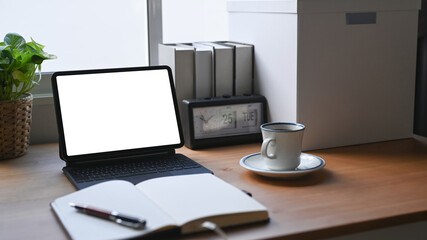 Comfortable workspace with computer tablet, notebook, coffee cup and books on wooden desk.