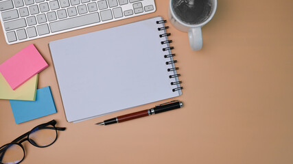 Top view empty notepad, coffee cup, sticky notes and glasses on .beige background.