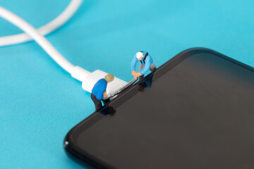 Miniature lumberjack prepares to saw off mobile phone charging cable - obrazy, fototapety, plakaty