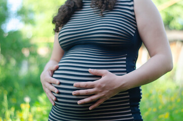 Silhouette of a pregnant woman in a striped dress with hands on belly